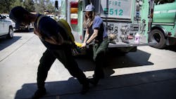 U.S. Forest Service firefighters Nick Browne (left) and Justine Gude deploy a Gasner hose pack during a training demonstration at the Oak Flat Fire Station on July 3 in Castaic, CA. The hose packs are fire hoses folded in a unique way enabling firefighters to carry the pack on their backs and deploy them in fighting wildfires.