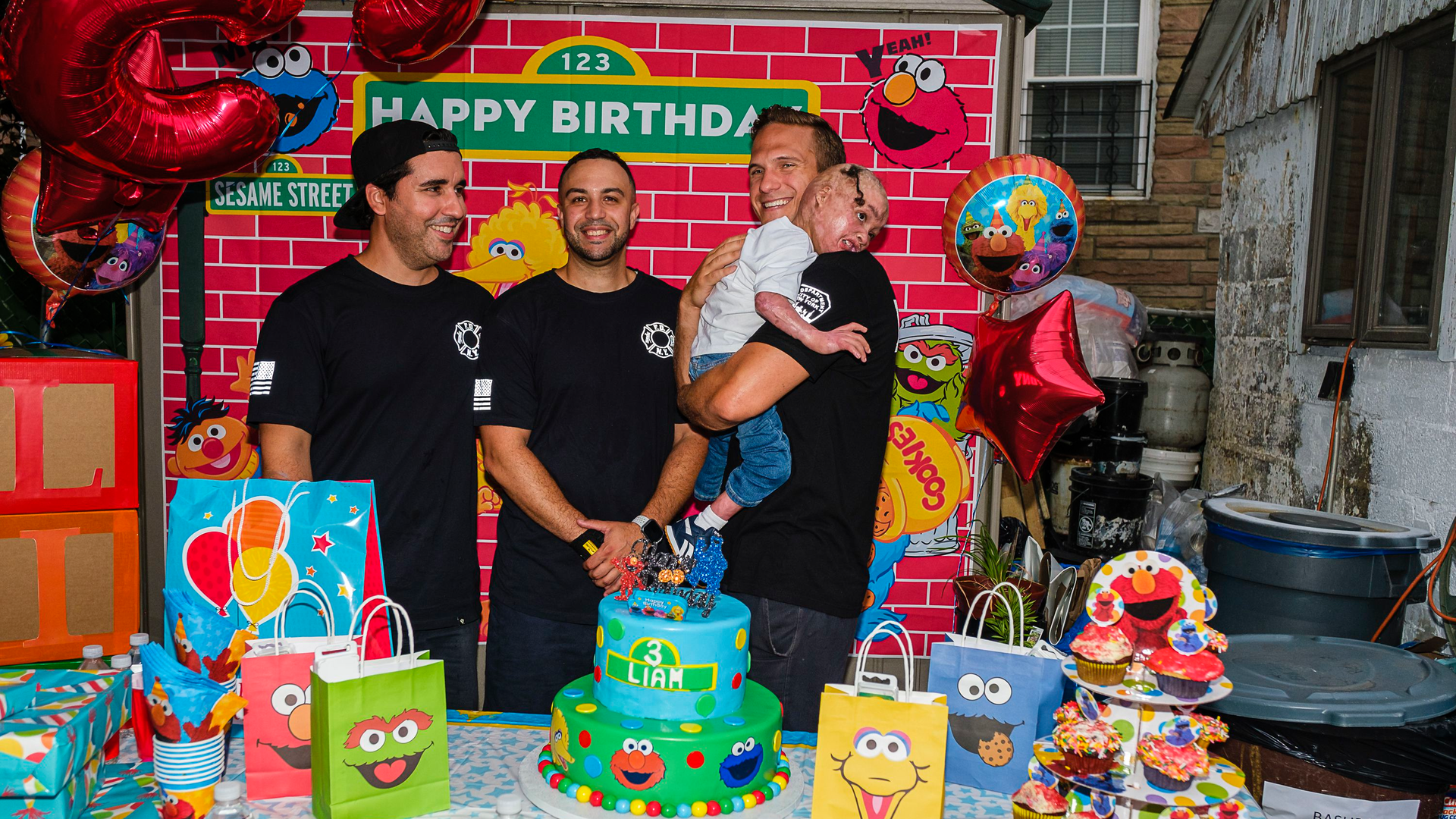 Firefighters Manuel Costa (left to right), Lawrence Young, and Steve Keenan, holding Liam Dominguez Rodriguez at Liam's third birthday party.
