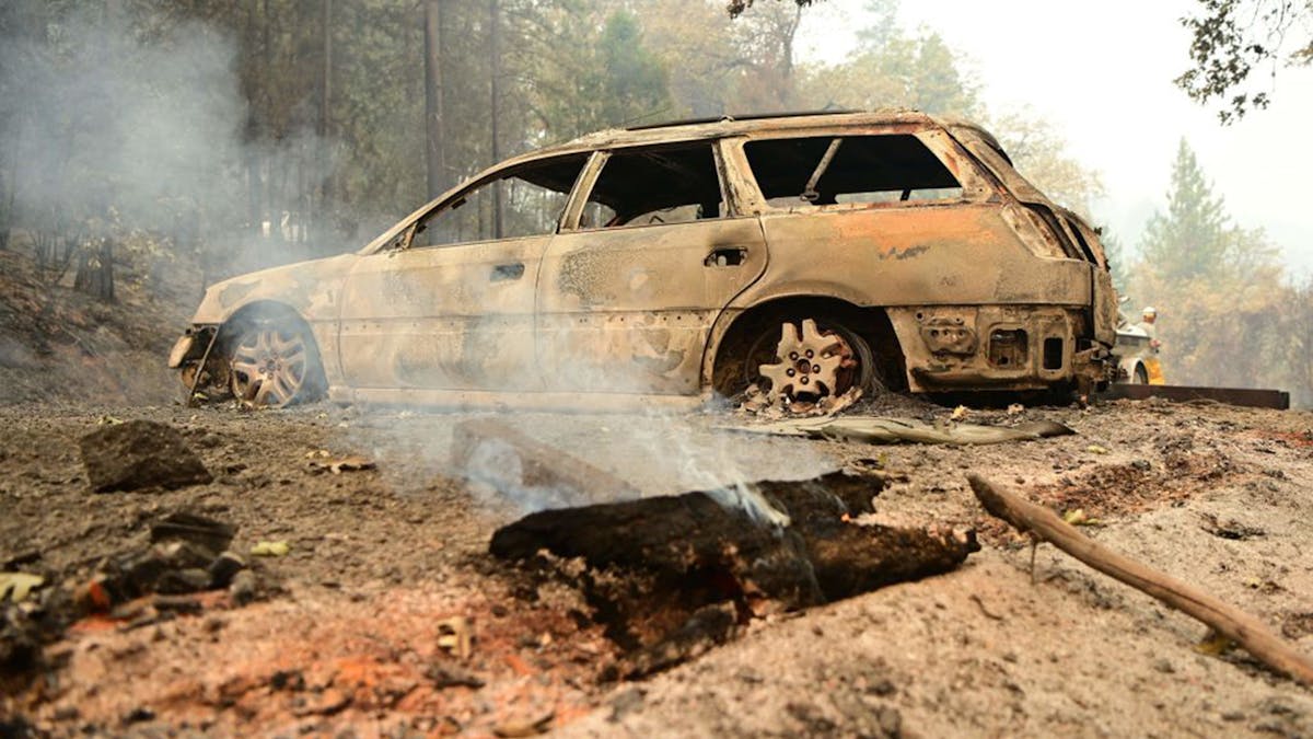 A log smolders in front of a burnt car at a property during the Salt Fire in the Gregory Creek area of Shasta County, south of Lakehead, CA, in July 2.