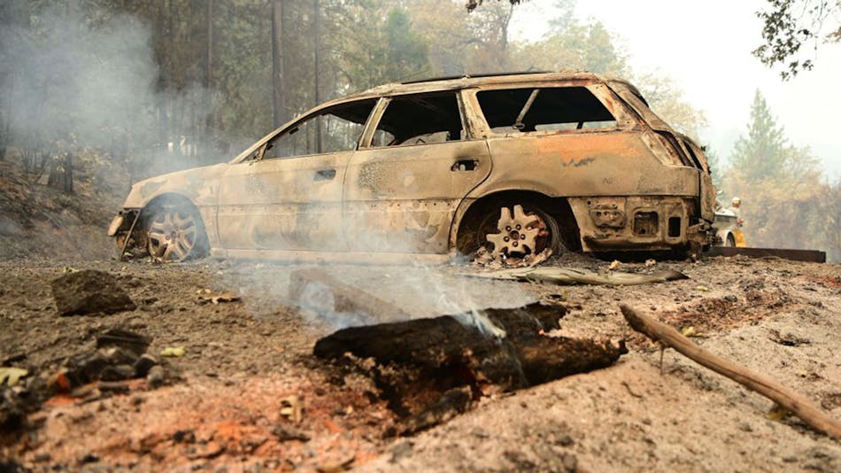 A log smolders in front of a burnt car at a property during the Salt Fire in the Gregory Creek area of Shasta County, south of Lakehead, CA, in July 2.