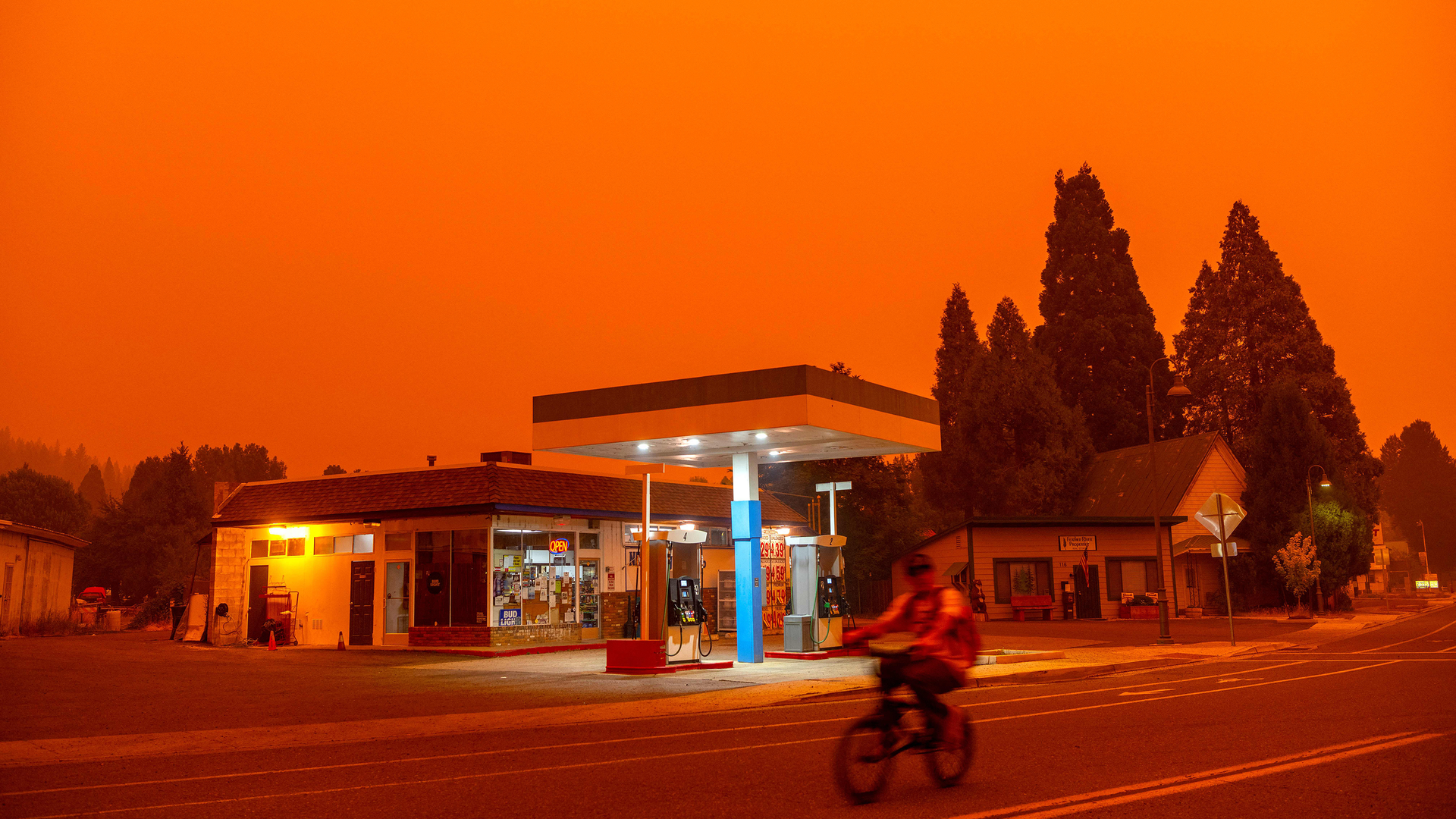 Smoke from the Dixie Fire fills the sky as a bicyclist rides past a gas station in Greenville, CA.