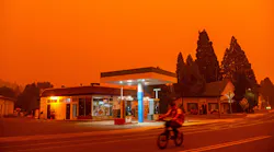 Smoke from the Dixie Fire fills the sky as a bicyclist rides past a gas station in Greenville, CA.
