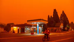 Smoke from the Dixie Fire fills the sky as a bicyclist rides past a gas station in Greenville, CA.