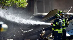 Firefighters wet down the area where a small plane crashed into a manufacturing building Thursday.
