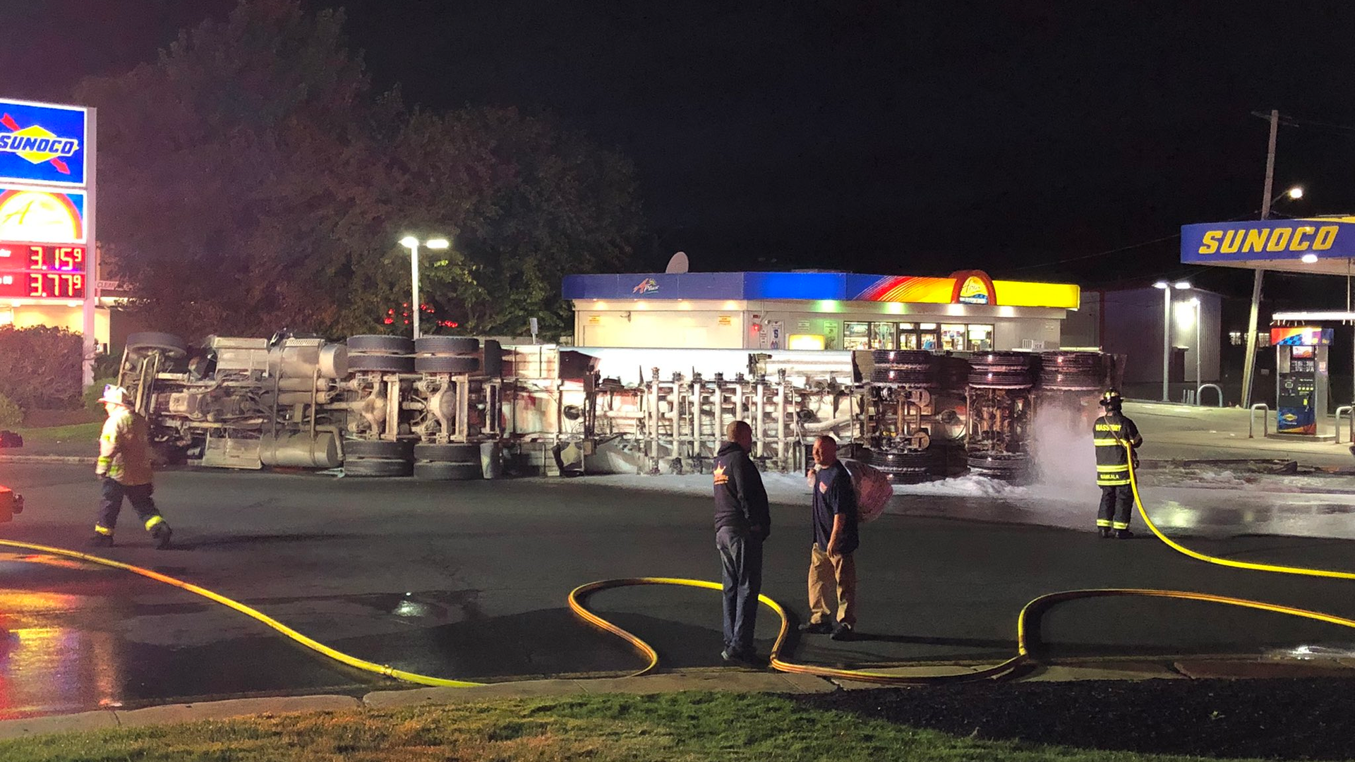 A firefighter (right) sprays suppression foam after a tanker rollover spilled 10,000 gallons of diesel fuel in Revere, MA, on Wednesday, Oct. 13, 2021.