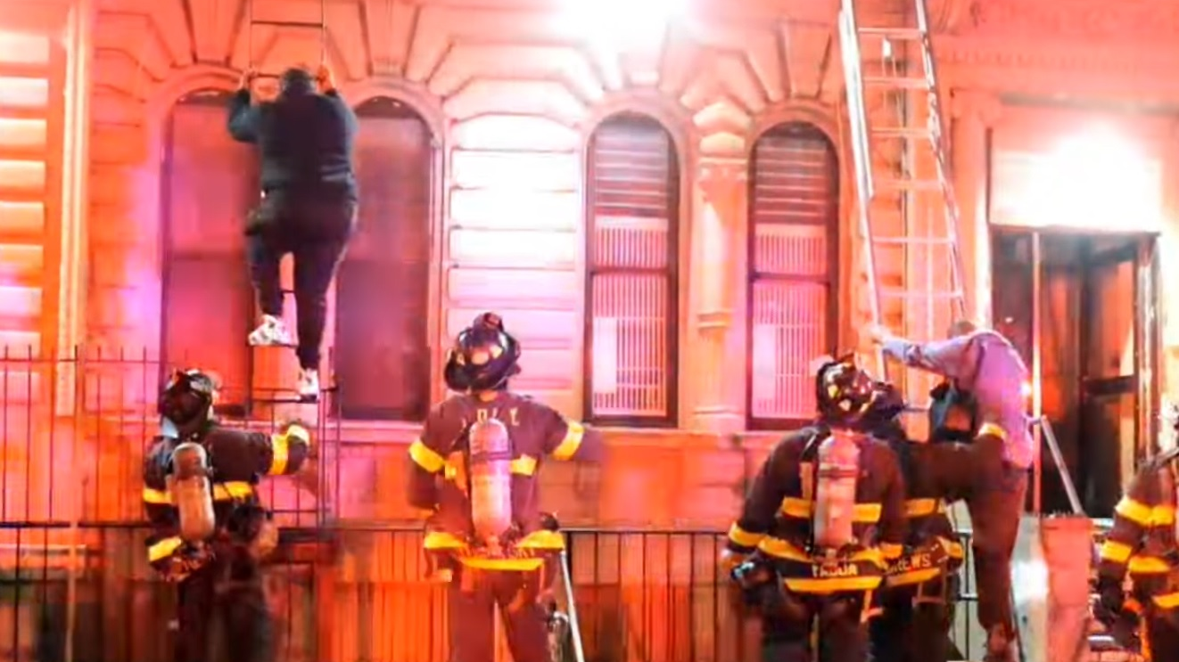 FDNY firefighters assist victims down fire escapes and ground ladders during a two-alarm fire in Harlem.
