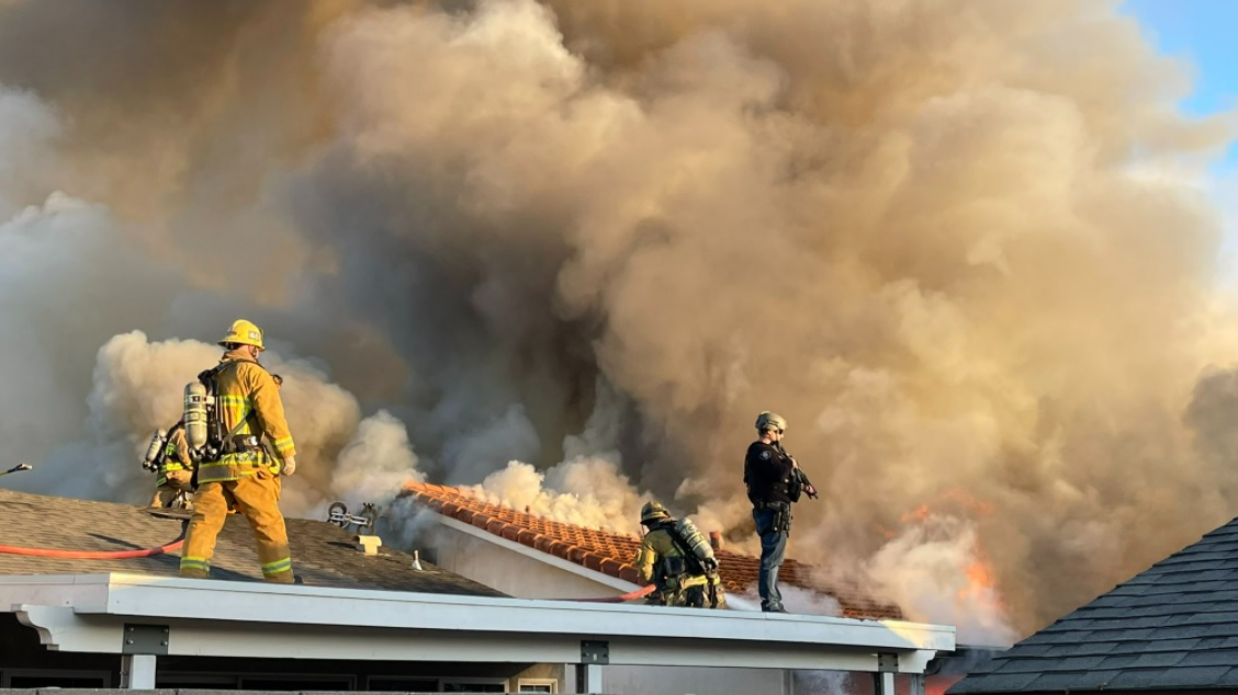 Police stand by with a rifle as Ventura County firefighters operate at a dwelling fire that was intentionally set.