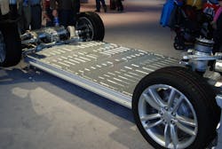 Shown is the floorpan-mounted, high-voltage lithium-ion battery pack of a Tesla Model S sedan. The completed body of the vehicle is placed onto this battery pack. The electric motor, shown at upper left, drives both rear-axle wheels.