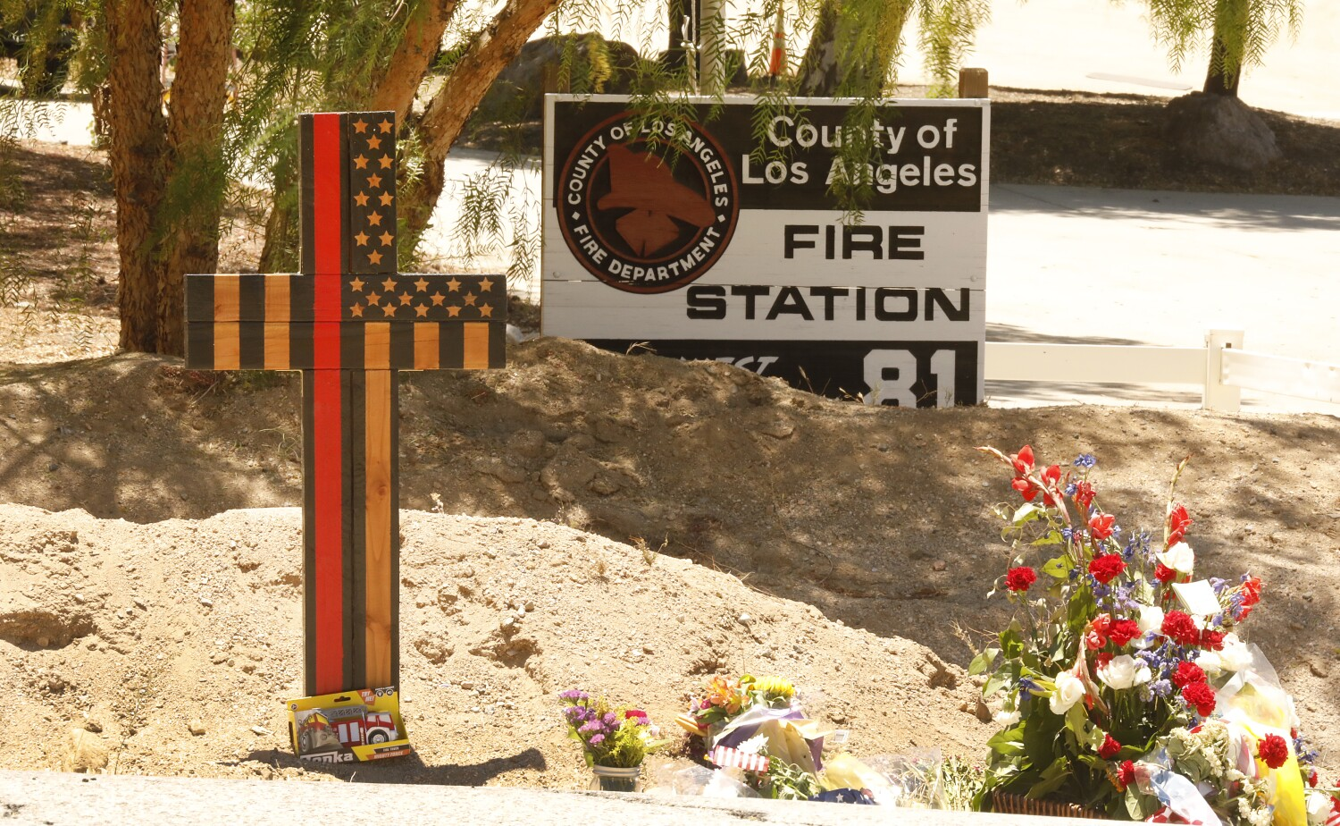 A memorial features a cross made of wood along with flowers outside of Los Angeles County Fire Dept. Station 81 in Agua Dulce where a Los Angeles County firefighter was killed in a shooting.