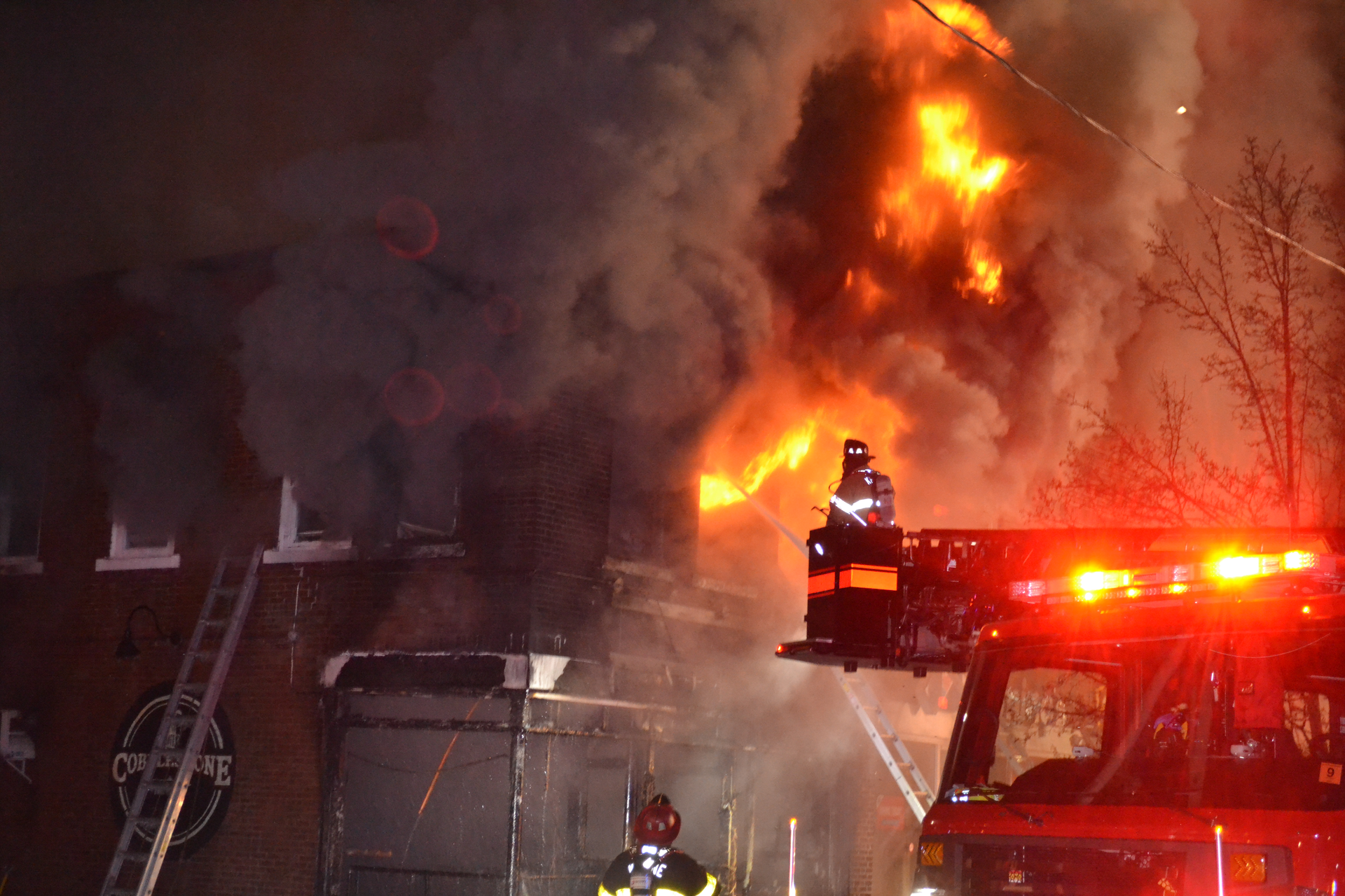 Fire spread upward rapidly and into the voids between the floors and the roof of a mixed occupancy, requiring the rescue of a resident from the second floor and a firefighter who lost his bearings amid clutter in an apartment.