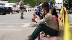 A sheriff checks his phone as he sits on the sidewalk outside Robb Elementary School in Uvalde.