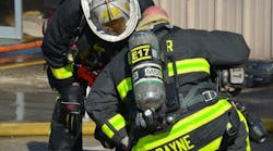 Firefighter Payne was working overtime on Engine 17. Notice the helmet under his right arm, with its changeable front piece with black letters. His name is on the bottom of the helmet. He&rsquo;s a firefighter, so his helmet is black, but his role as acting as officer for the day is signified by the white front piece.