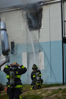 A firefighter from the RIT engine company applies water to the soffit and attic and off of the ceiling of the original fire room without causing any concern to the interior crews that were delayed getting to the room.