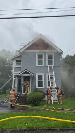 Firefighters operate as smoke pours from the structure. Hoses were brought into the house from doors in the front and rear of the home. In the center of this picture, firefighters place a ladder for emergency escape from the second floor if needed.