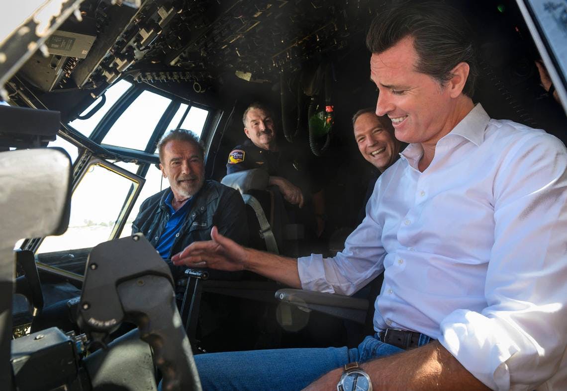California Gov. Gavin Newsom, right, and former Gov. Arnold Schwarzenegger talk in a C-130 airplane cockpit with Cal Fire personnel at McClellan Airport near North Highlands in 2019.
