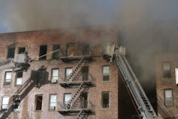 Tower ladders operate their streams into the top floor of a large, six-story, multiple dwelling during a five-alarm fire, where heavy fire and smoke vented from the top floor and roof.