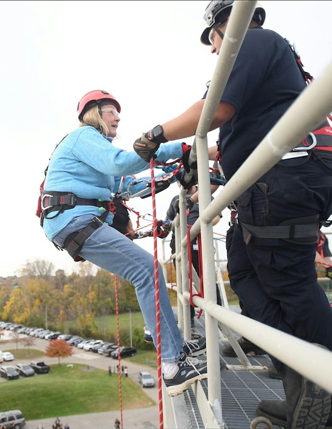 Firefighter Paul Semaan helps Michigan House of Representatives Denise Mentzer over the edge to rappel down the live burn tower at Macomb Community Colleges Public Service Institute.