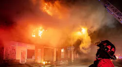 A Fort Worth firefighter surveys the scene as flames engulf a vacant warehouse.