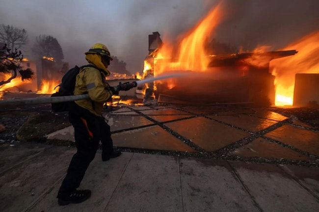 A firefighter sprays water on the Palisades fire in Pacific Palisades Tuesday.