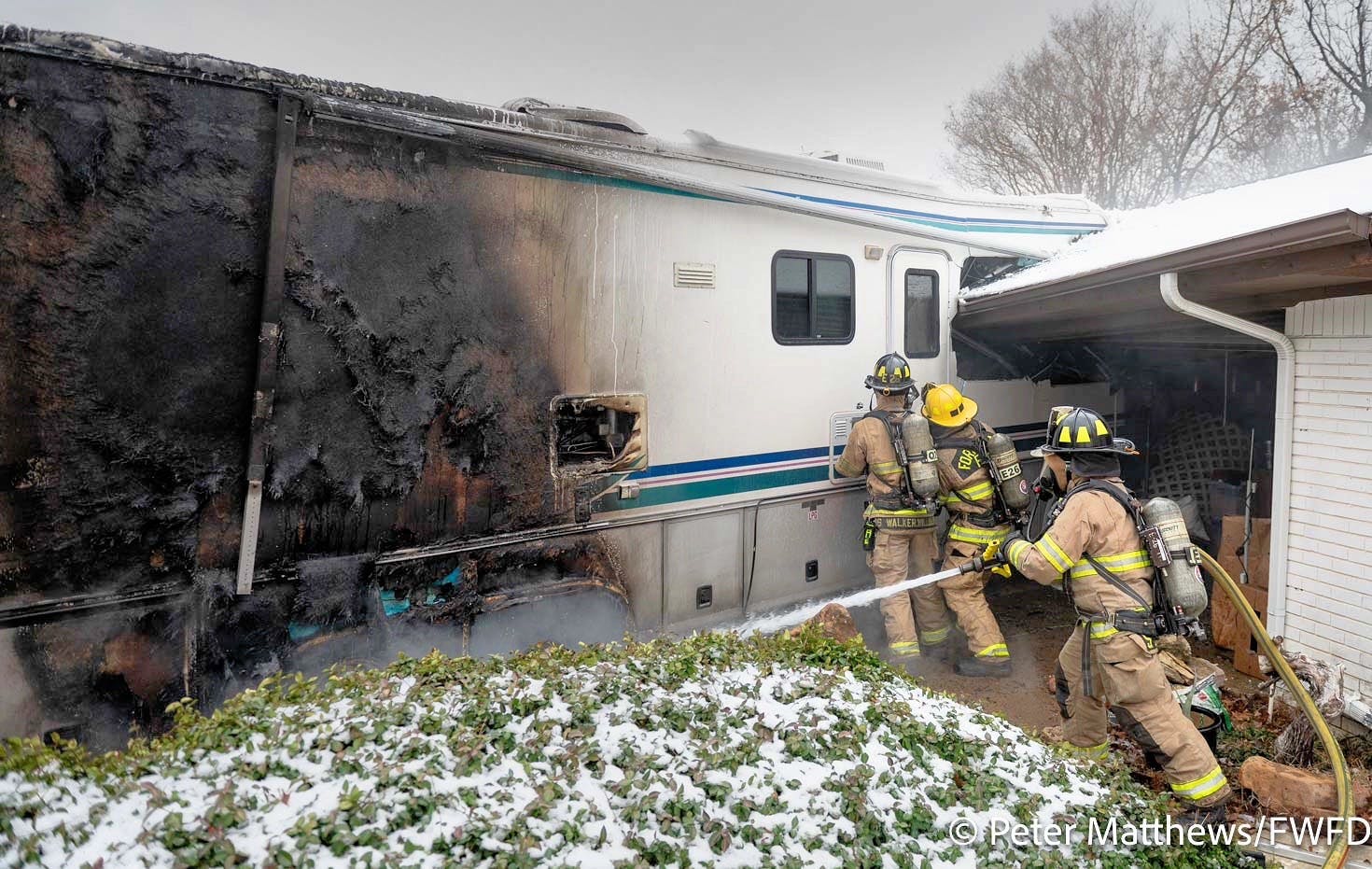Fort Worth firefighters work to gain access to the interior of the RV while a firefighter douses the fire.