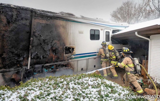Fort Worth firefighters work to gain access to the interior of the RV while a firefighter douses the fire.