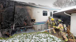 Fort Worth firefighters work to gain access to the interior of the RV while a firefighter douses the fire.