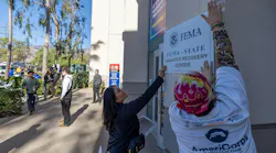 Workers put up a sign as wildfire victims seek disaster relief services at one of two FEMA Disaster Recovery Centers in Pasadena.