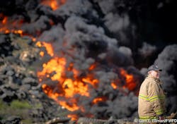 A Fort Worth firefighters watches over the scene as a large pile of tires and other debris burns in the background. A Fort Worth firefighters watches over the scene as a large pile of tires and other debris burns in the background.