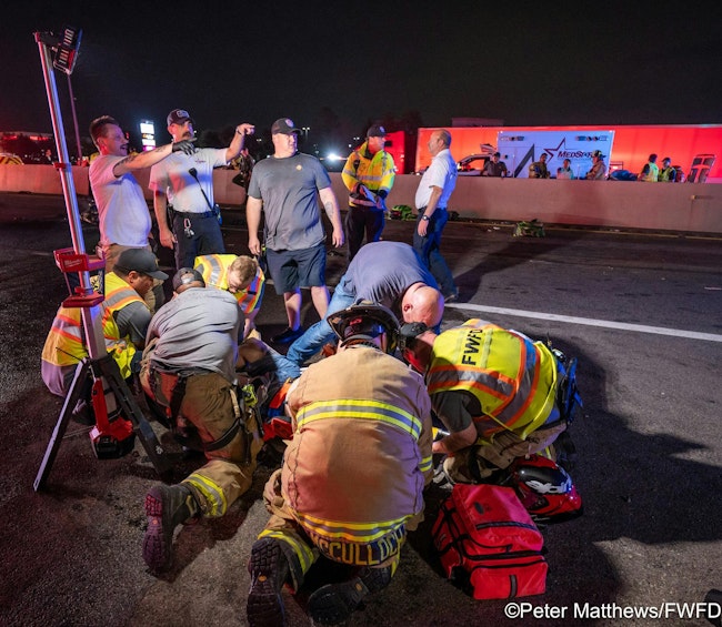 Fire and EMS personnel coordinate patient transportation in the background as firefighters and paramedics provide treatment to a patient.