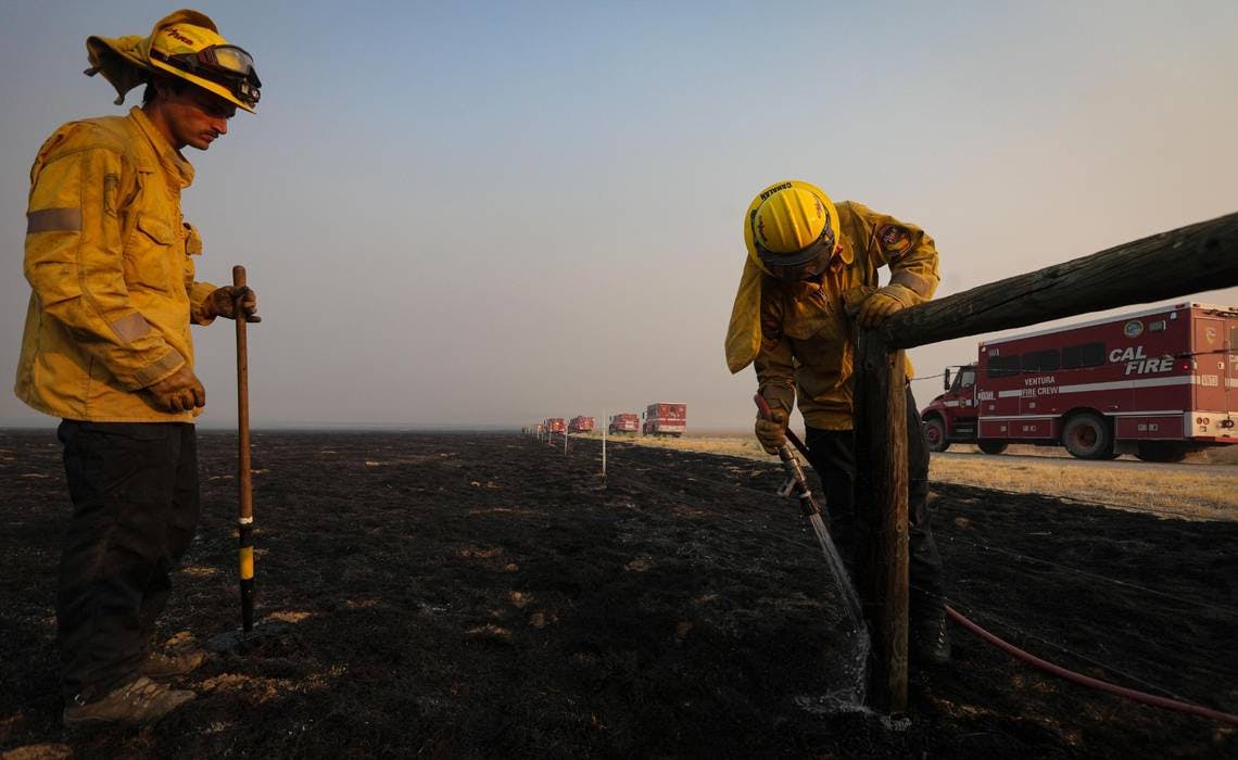Monterey County firefighters Jonathan Davis, left, and Ryan Cahalan extinguish smoldering wood posts on a cattle fence after the Madre Fire burned through the area on July 3.