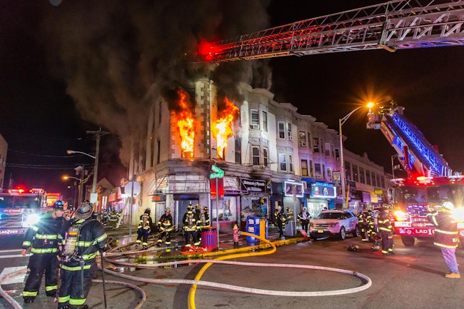 First-arriving Passaic Fire Department crews reported heavy smoke showing from first-floor stores and upper-floor apartments of a three-story mixed occupancy. Heavy fire in one store prompted a second alarm. During search operations, Ladder 1 reported heavy fire in the ceiling. A third alarm was transmitted, which brought mutual aid from Bergen and Essex counties. With four lines operating, crews removed several occupants. With heavy fire visible on the second floor and thick, black smoke pushing from the second and third floors, command ordered all companies out and transitioned to a defensive attack.