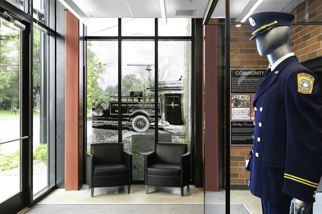 The 24/7 lobby of Arlington County, VA, Fire Department Fire Station 8 includes panels that are designed around the six community virtues that emerged from meetings that included members of the community. Artifacts that were donated by the Halls Hill community include a full dress uniform and photographs from family and department archives. An image of the original Halls Hill Volunteer Fire Department water tank aboard the back of its first engine was installed on the glass, so the community can see the fire station and members can see the community through the lens of history.