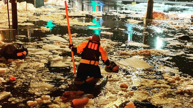 A flood-rescue technician removes a hazard from the roadway during nor&rsquo;easter flooding.