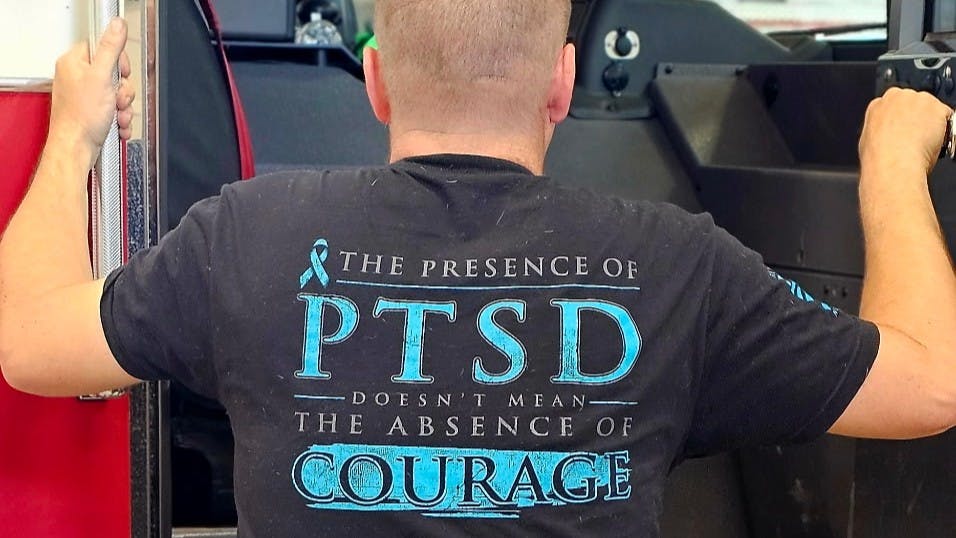 firefighter addressing mental health issues wearing a T-shirt that reads 'The presence of PTSD doesn't mean the absence of courage'
