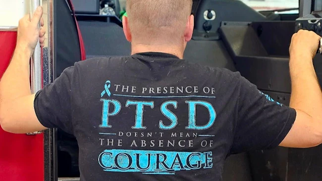 firefighter addressing mental health issues wearing a T-shirt that reads 'The presence of PTSD doesn't mean the absence of courage'
