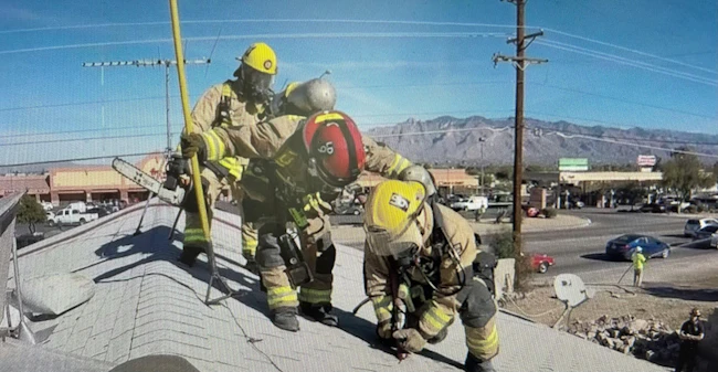 firefighters on a roof deploying a piercing nozzle to put water on an attic fire that's below them