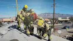firefighters on a roof deploying a piercing nozzle to put water on an attic fire that's below them