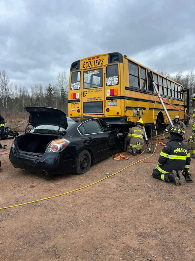 firefighters training scenario involving school bus on top of automobile