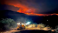 A dozer clears debris as fire burns in the mountains, serving as a remidner that wildfire responses require multiple resources and assets.
