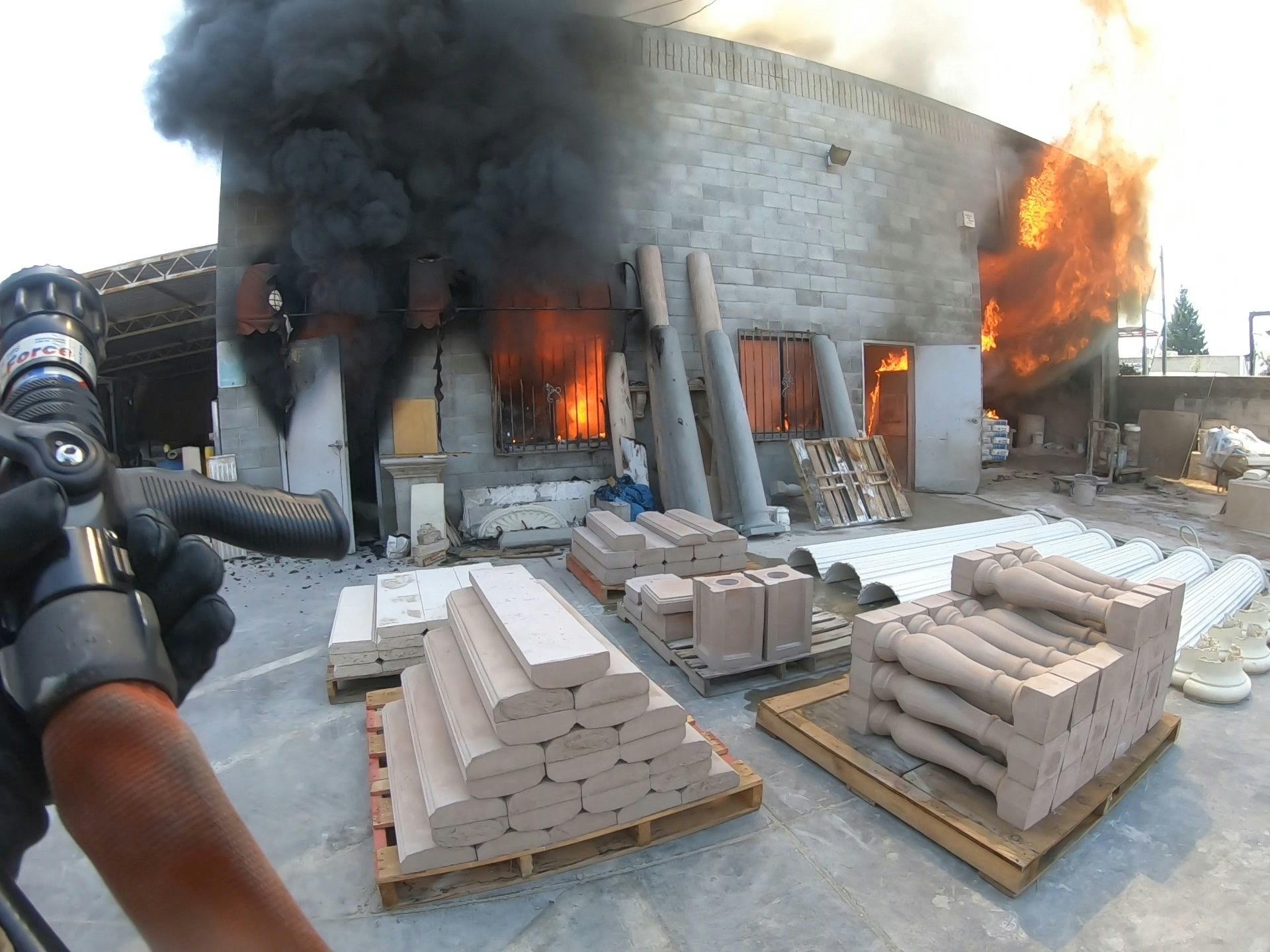 firefighter approaching building fire with hose in hand