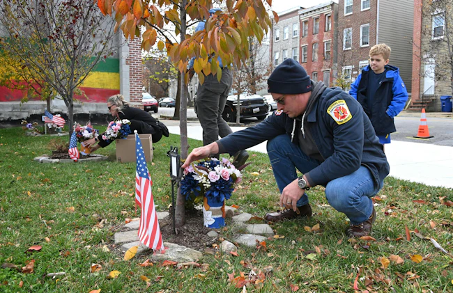 Baltimore Firefighter Kyle Higley and his son, Parker along with Lacey Marino, sister of Lt. Kelsey Sadler, place flowers at the Stricker Street Fire Memorial.