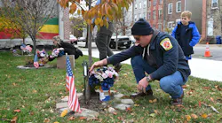 Baltimore Firefighter Kyle Higley and his son, Parker along with Lacey Marino, sister of Lt. Kelsey Sadler, place flowers at the Stricker Street Fire Memorial.